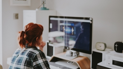 Red-haired woman in checkered shirt working at desktop computer.